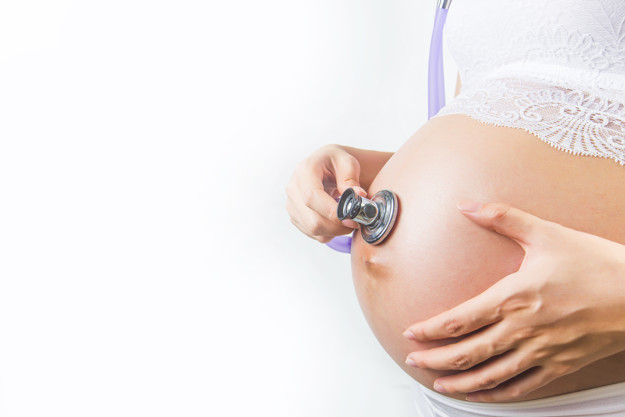 Pregnant woman using stethoscope examining on her baby in her be