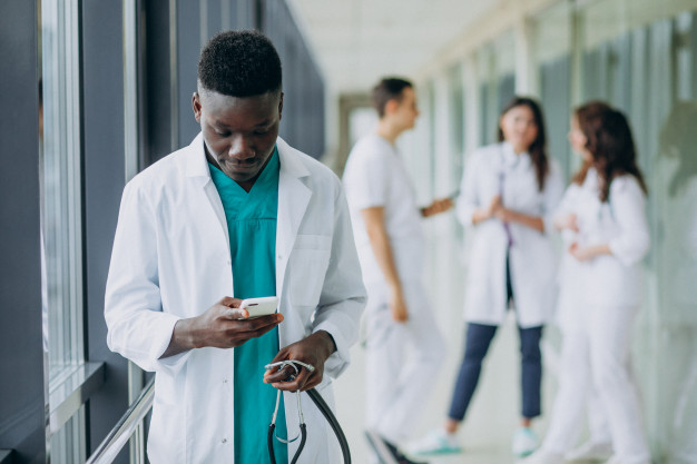 medico americano africano homem usando o smartphone no corredor do hospital