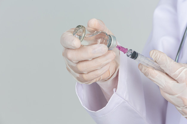 jovem medico esta segurando a seringa hipodermica com luvas de borracha do frasco de vacina na parede cinza