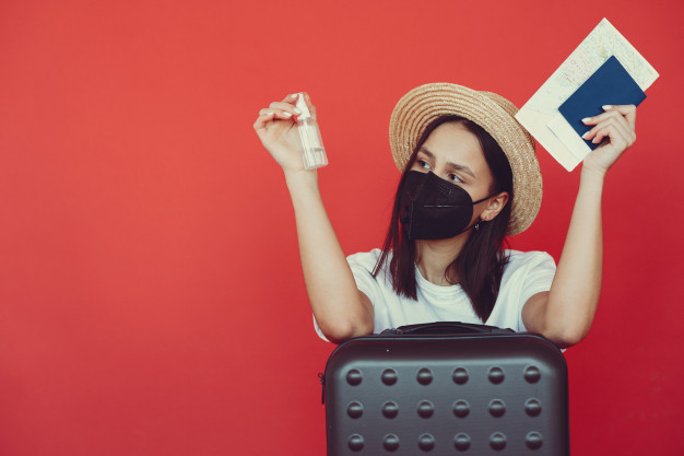 menina elegante posando com equipamento de viagem em uma parede vermelha