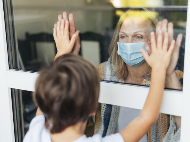 mulher com mascara medica cumprimentando o sobrinho pela janela