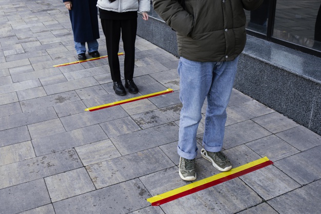 pessoas na fila esperando atras da faixa de distancia social