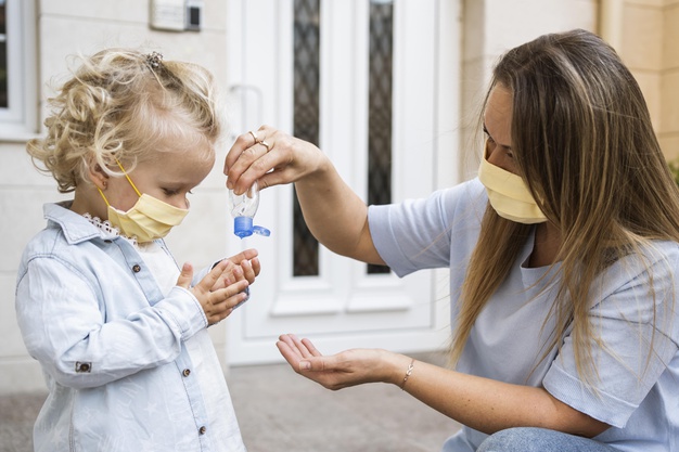 vista lateral de mae e filho com mascaras medicas e desinfetante para as maos