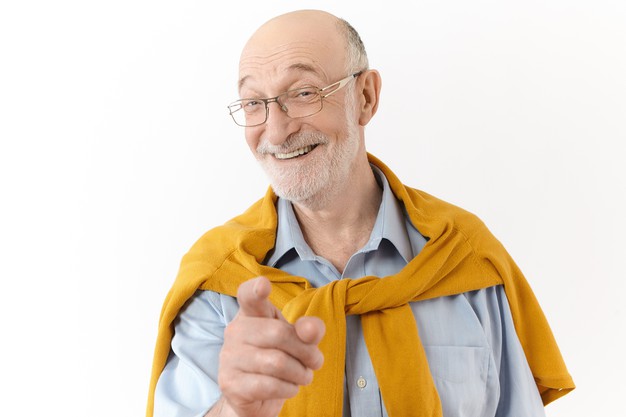 foto de um homem senior bonito emocional com cabeca careca e barba por fazer sorrindo amplamente e apontando o dedo indicador para a camera rindo de uma historia engracada ou piada po