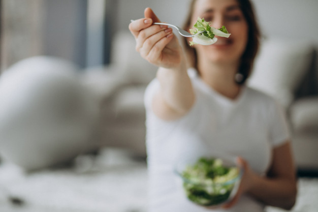 jovem mulher gravida comendo salada em casa