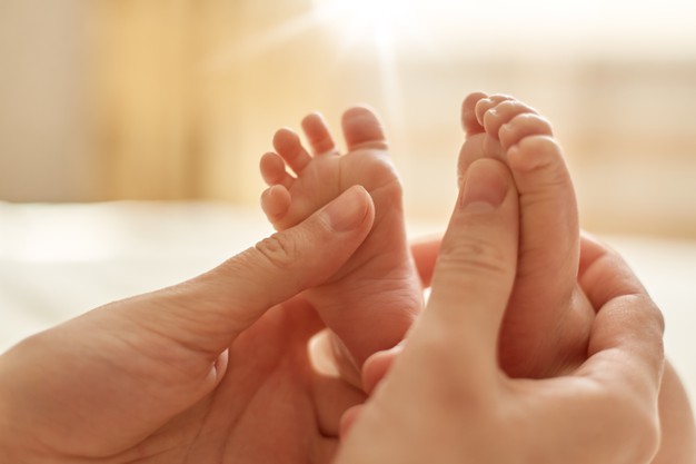 mamae fazendo massagem para bebes mae massageando os pes descalcos infantis massagem preventiva para recem nascidos mamae acariciando os pes do bebe com as duas maos sobre fundo claro