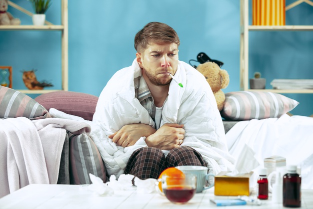 homem barbudo doente com gripe sentado no sofa em casa e medindo a temperatura corporal o inverno a doenca a gripe o conceito de dor relaxamento em casa conceitos de saude