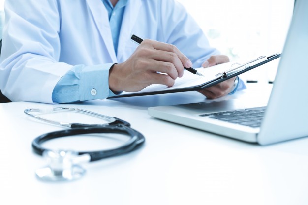 medico trabalhando com laptop e escrevendo na papelada fundo hospitalar