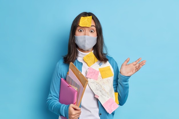mulher empreendedora intrigada e hesitante trabalha longe de casa estando em auto isolamento usa mascara protetora de coronavirus sobrecarregada com papelada e organiza a programacao