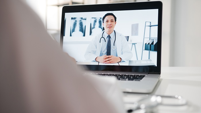Young Asia male doctor in white medical uniform using laptop tal