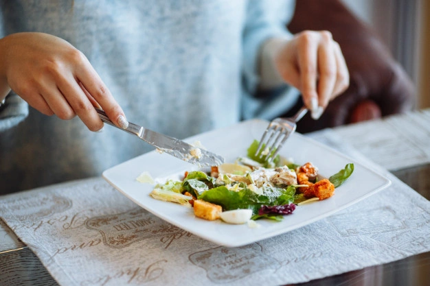 maos de mulher com salada caesar na mesa no restaurante