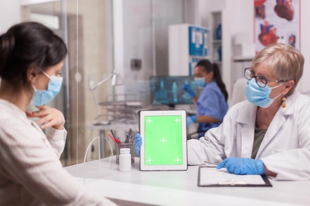 medico com mascara facial olhando para o tablet com tela verde durante a consulta com paciente doente enfermeira de uniforme azul