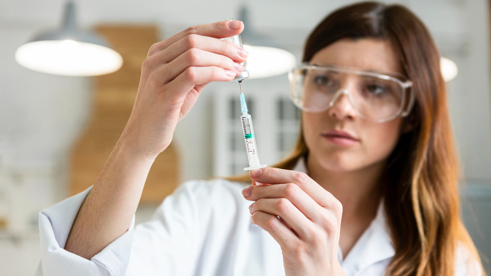 female scientist with safety glasses holding syringe with vaccine
