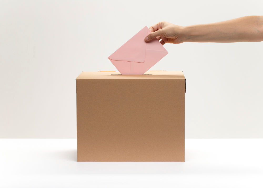 hand puts pink envelope into vote box