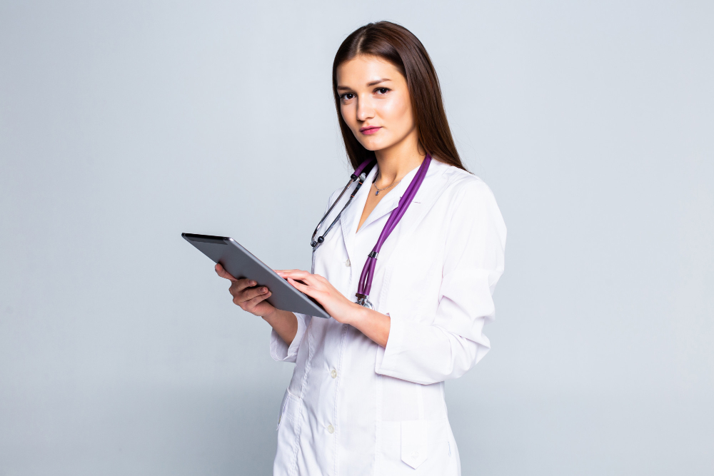 smiling young woman in sweater scarf using tablet pc computer making video call isolated on grey wall healthy lifestyle online treatment consulting cold season concept