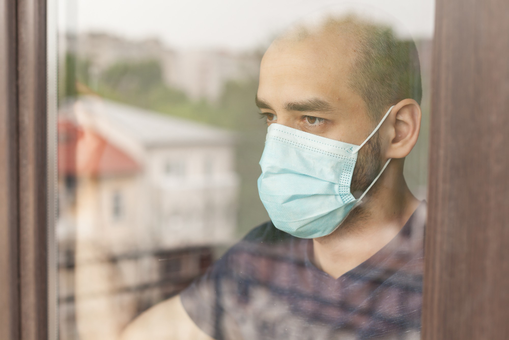 serious man looking outside through windos glass during quarantine wearingglass d