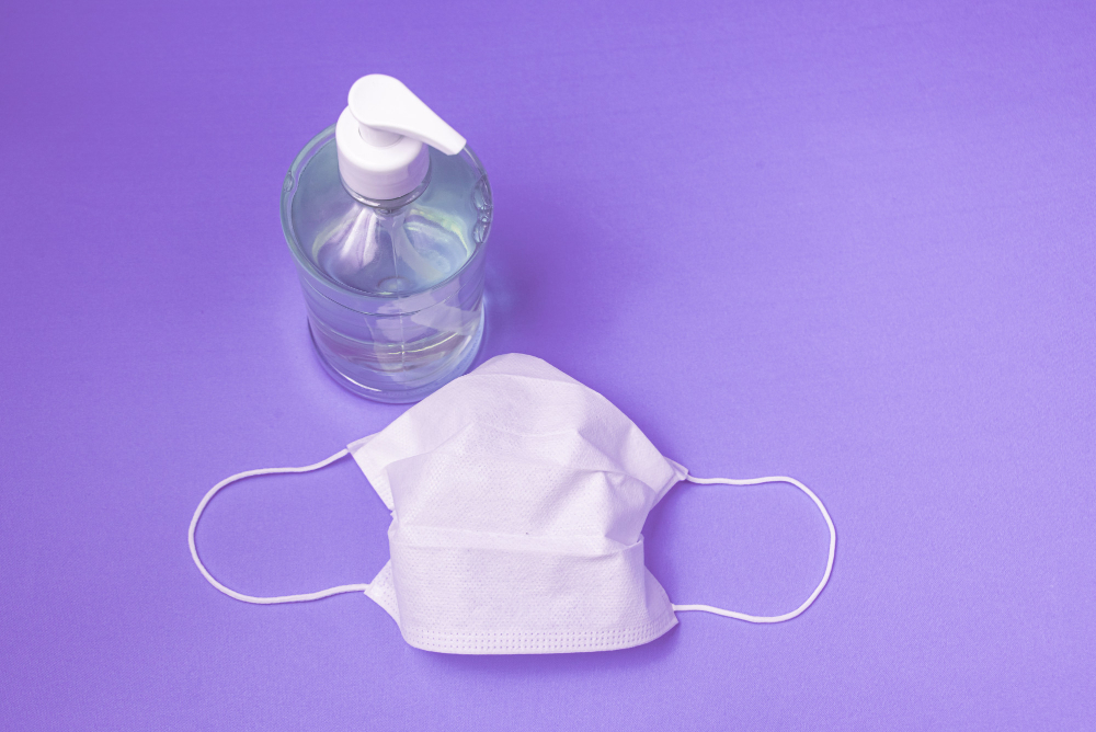 container with alcohol gel and surgical mask on the light blue