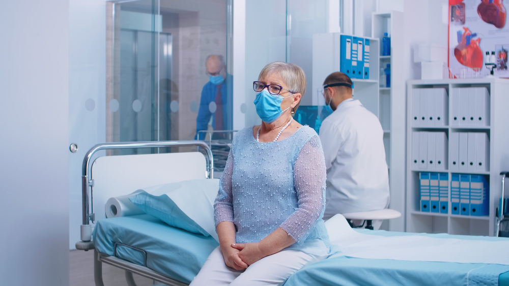 portrait of elderly lady sitting on the hospital bed during covid crisis doctor and patients wearing protective mask and equipent in modern private cinic healthcare system after coronavirus