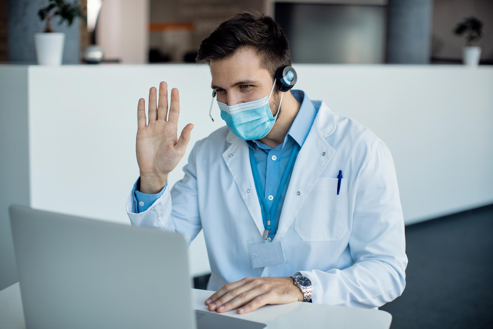 male doctor waving during a video call over laptop at medical clinic