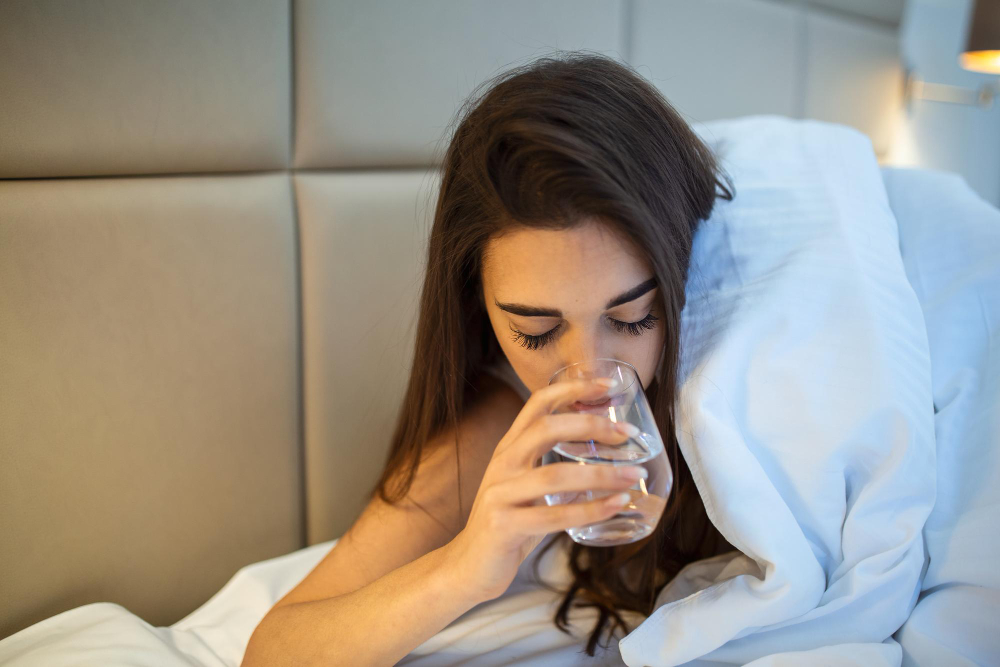young woman drinking glass of water in bed at night woman drinking a glass of water before going to sleep she is lying in bed