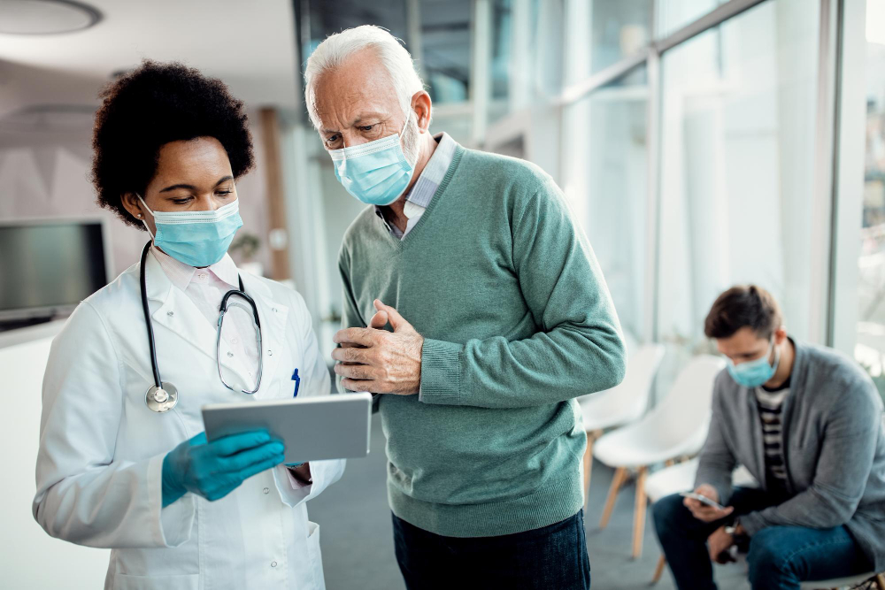 black female doctor and senior man using touchpad while wearing face masks at medical clinic