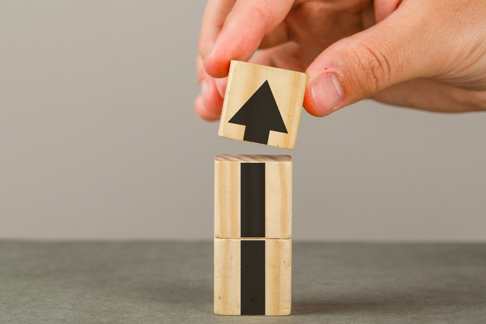business growth concept on grey and white wall side view hand putting wood block onto tower