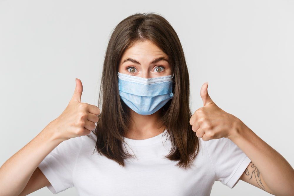 covid health and social distancing concept close up of pleased attractive girl in medical mask showing thumbs up in approval