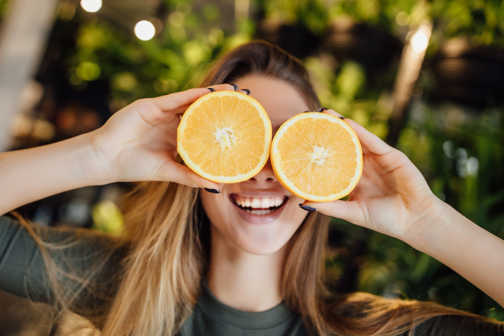 happy young caucasian woman holding fresh oranges in front of eyes and smiling
