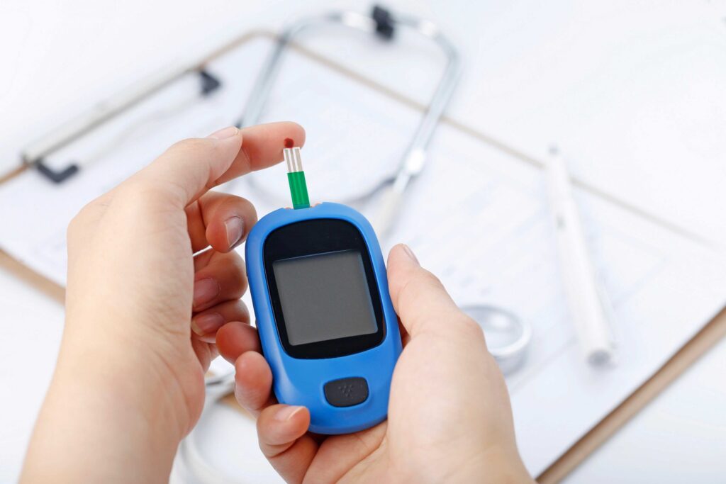 hand holding a blood glucose meter measuring blood sugar the background is a stethoscope and chart file