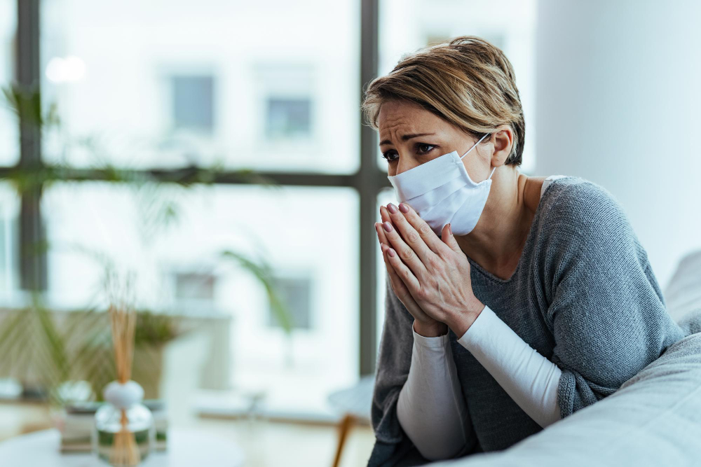 worried woman praying with hands clasped while wearing protective face mask and feeling sad during coronavirus pandemic