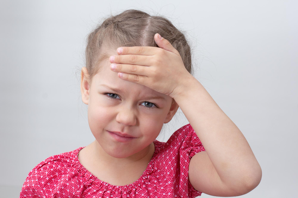 child with headache holding hand forehead