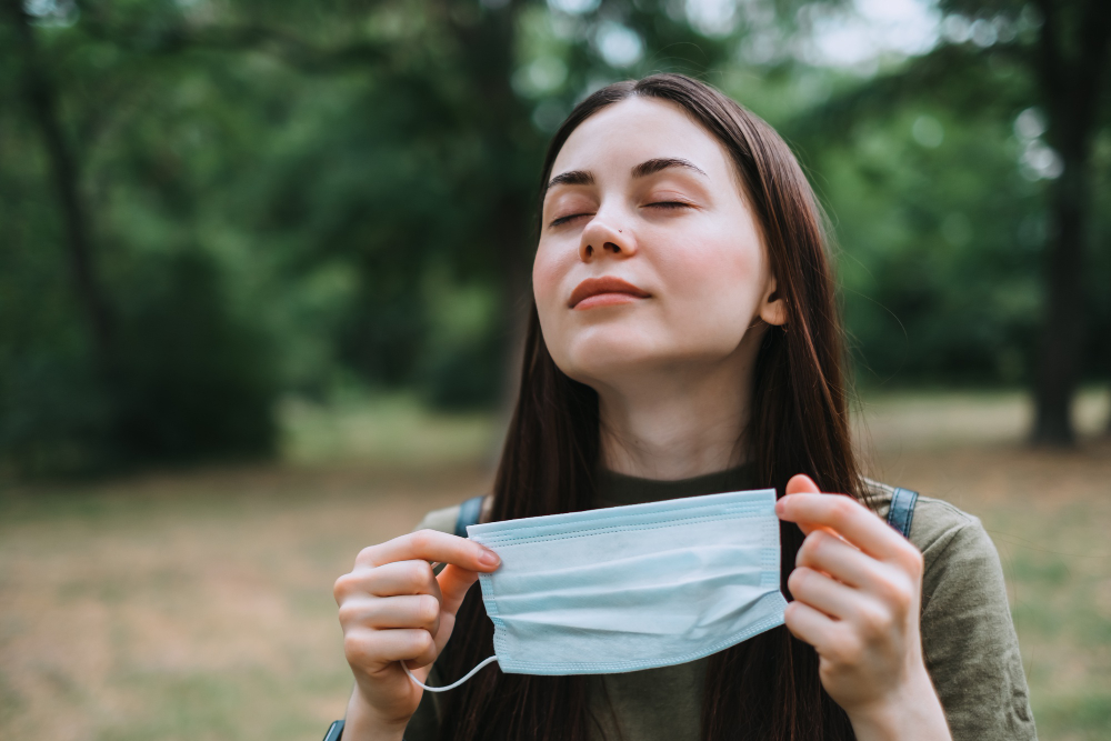 young caucasian pretty woman removes a medical protective mask on nature breathing clean fresh air