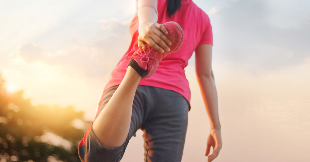 young woman runner stretching legs before running sunset rural trail