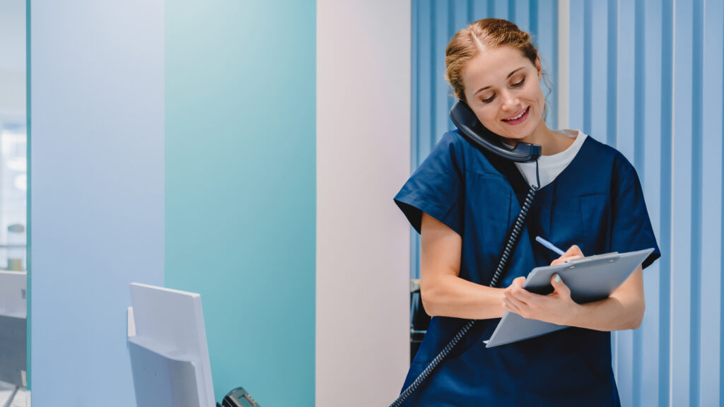 Caucasian female practitioner working at reception desk while answering phone calls and scheduling appointments in medical clinic