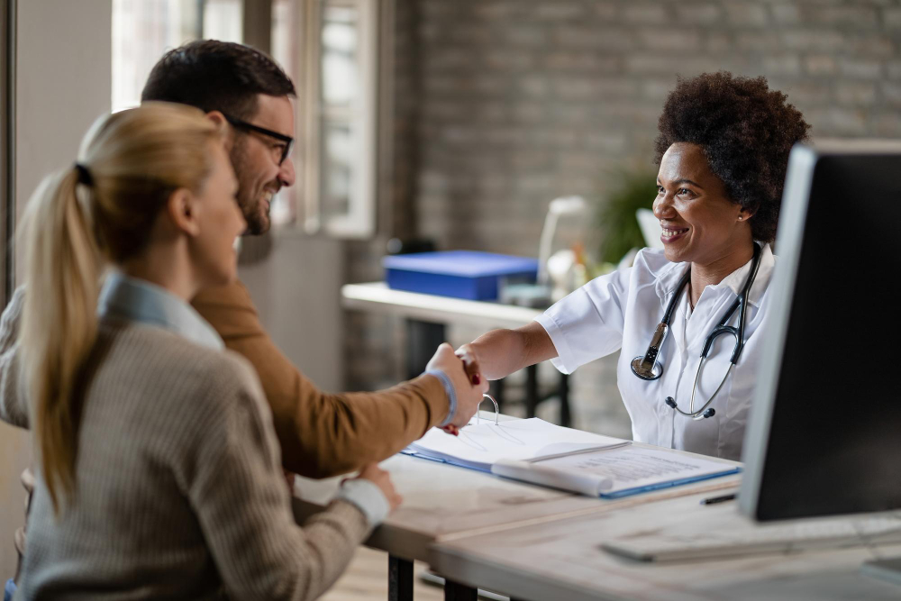 casal feliz apertando as maos com medica negra apos as consultas na clinica o foco esta no medico