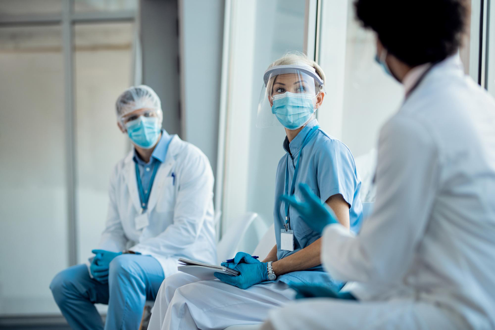 group healthcare workers with protective workwear talking while sitting hallway medical clinic