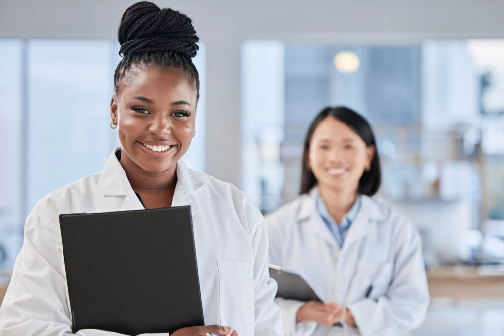 Doctor black woman, checklist and portrait with smile, planning and happy at clinic with asian expert Medic, teamwork and clipboard for schedule, analysis and results in hospital for health vision